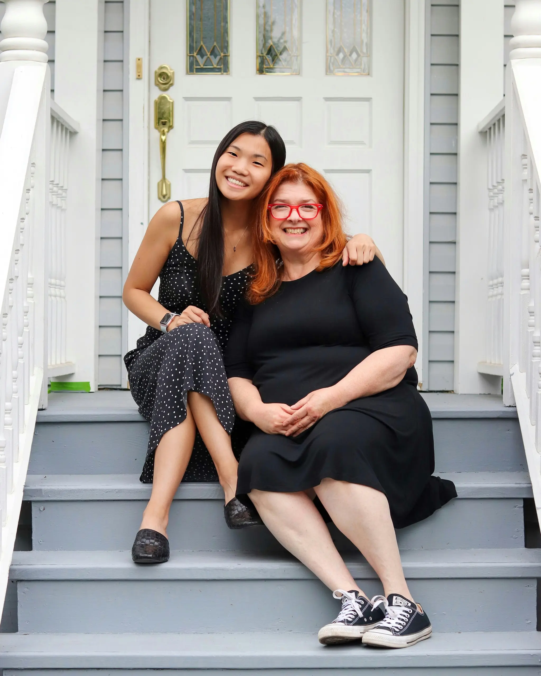 Two women laughing together on the front steps of a house